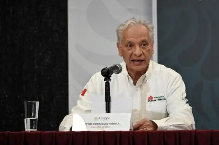 Man in a white shirt speaks into a microphone at a panel, with a glass of water and nameplate reading Victor Rodríguez Padilla, Director General PEMEX