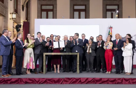 Group of officials on a stage, clapping as two people hold an open certificate during a signing ceremony.