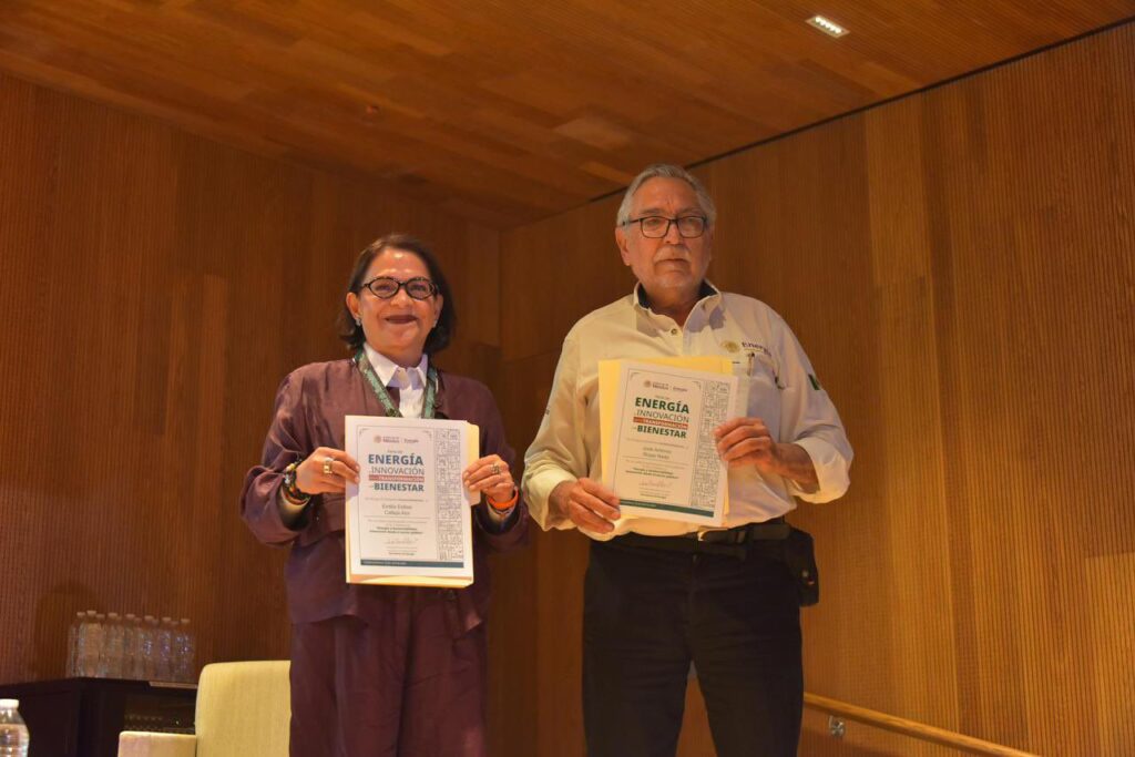 54e2a27b-a11e-4873-9549-16ab1767265c - Petróleo y Energía Two award recipients stand on a wood-paneled stage, each holding a certificate titled 'Energía Innovación Bienestar'.