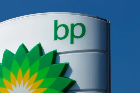 BP branding on a curved white sign with a green lowercase 'bp' and sunburst logo, against a clear blue sky.