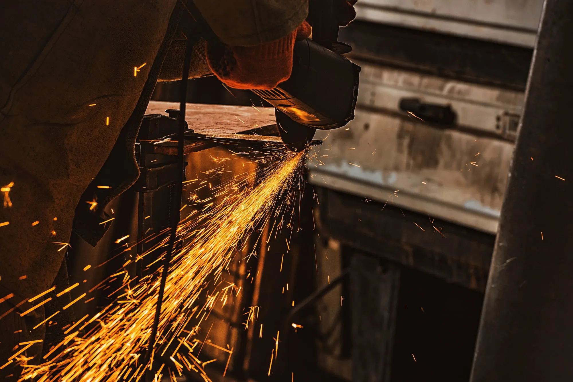 Worker in protective gloves grinding metal, sparks flying in a dim workshop