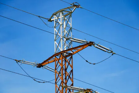 Orange and white steel transmission tower with insulators and high-voltage lines against a clear blue sky.