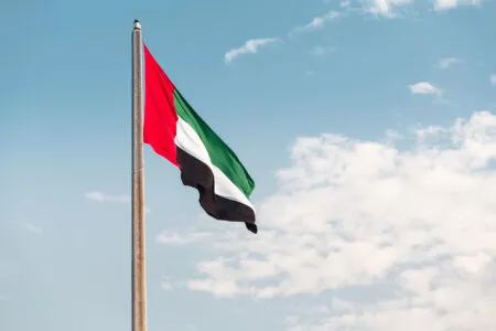 UAE flag waving on a tall flagpole against a clear blue sky.