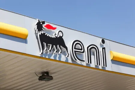 Close-up of a storefront sign featuring a black rooster logo with a red comb and partial bold letters against a blue sky.