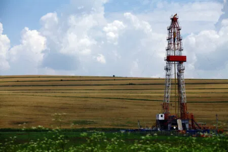 Oil drilling rig standing in a golden harvested field under a blue sky with white clouds.