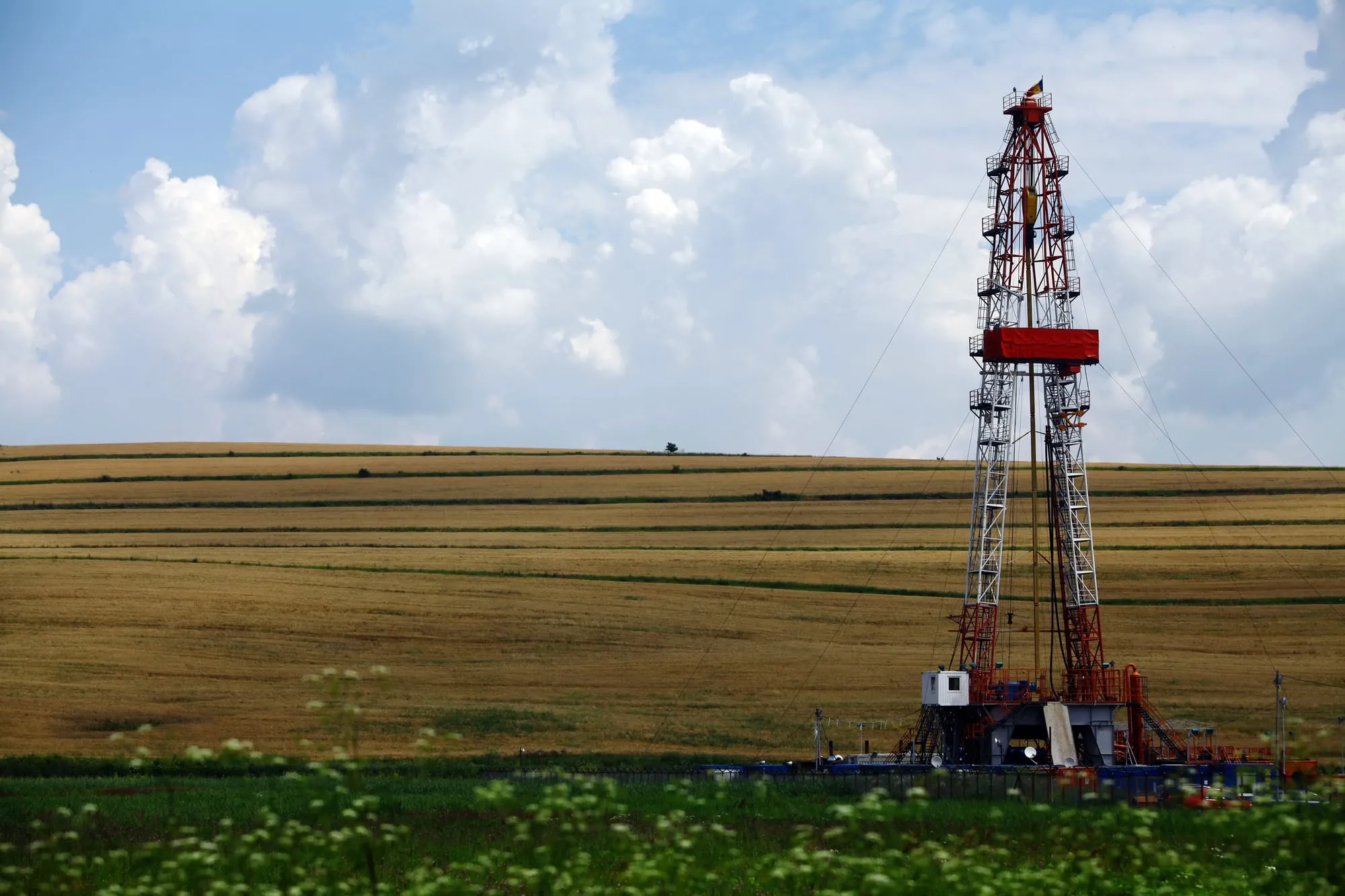 Oil drilling rig standing in a golden harvested field under a blue sky with white clouds.
