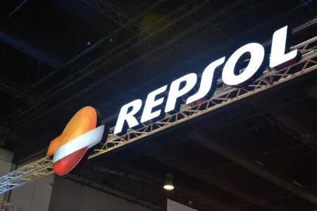 Repsol brand sign on a metal truss at an expo, with the white 'REPSOL' text beside an orange-red circular emblem with a white stripe, illuminated.