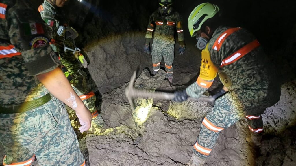 HG3-VRJXEAAmYnB - Petróleo y Energía Rescue team in camo and safety gear hammers at cracked rock floor inside a dark cave, with helmets and headlamps on.