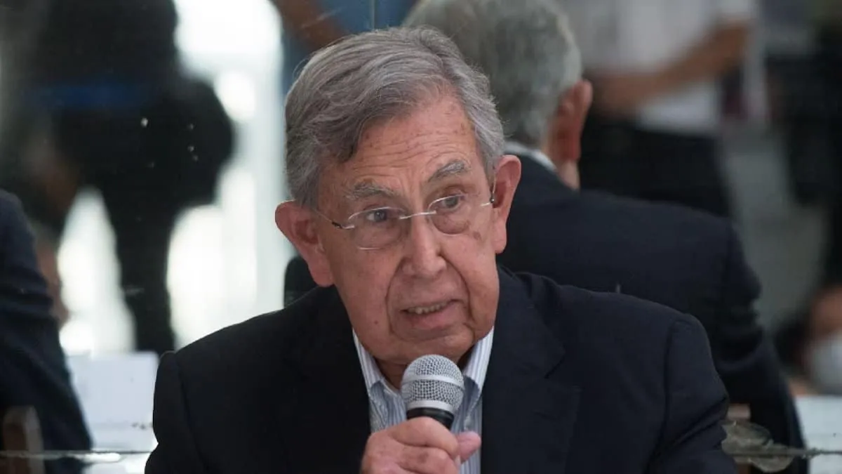 An older man in a suit speaks into a handheld microphone at a formal event.