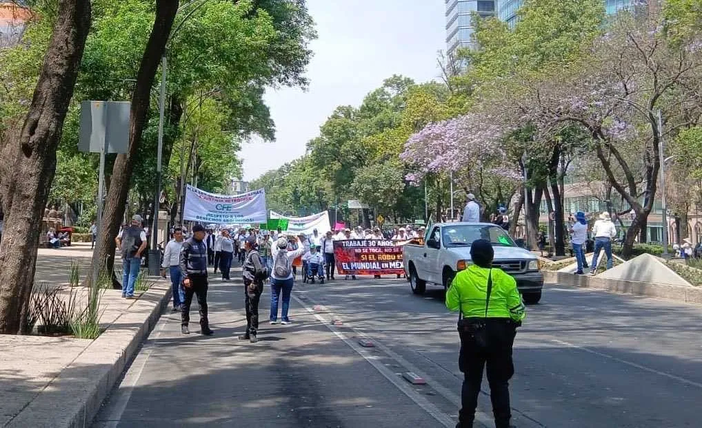 Protest march down a city street with banners held by a crowd, officers and bystanders on the sides; a pickup truck in the middle of the road.