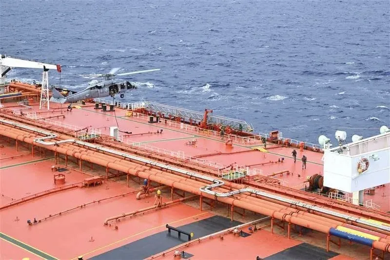 Red offshore platform deck with a helicopter parked near the edge and orange pipelines spanning the surface, ocean in the background.