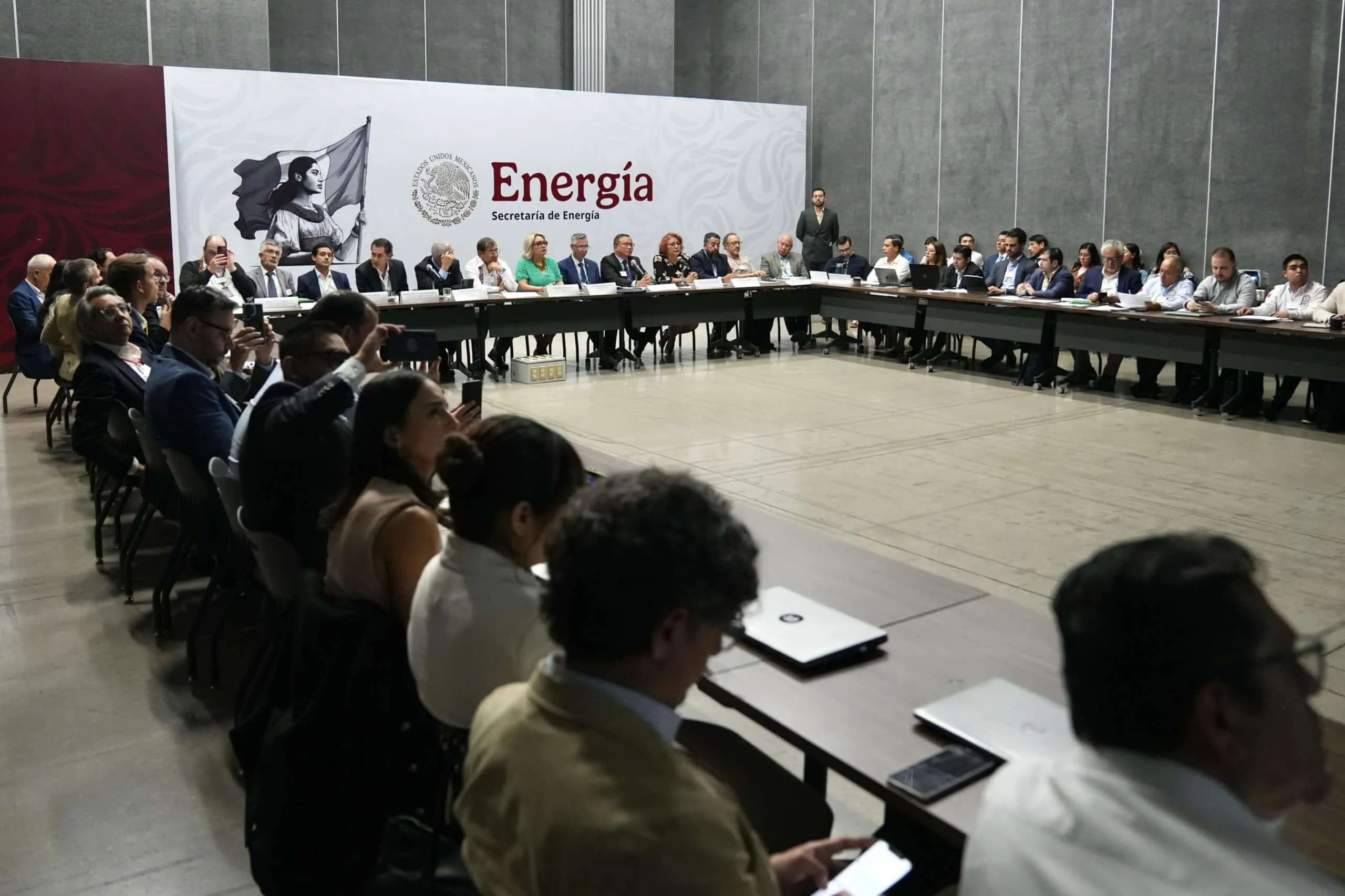 Group of professionals seated around a long U-shaped conference table during a formal meeting, with a large 'Energia' banner in the background.