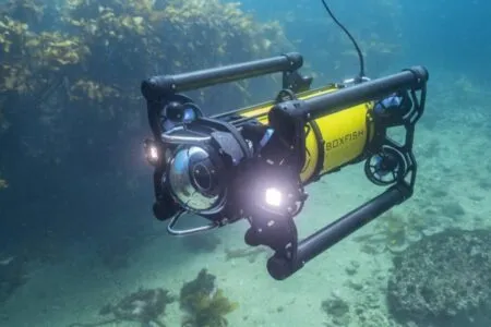 Yellow underwater ROV named Boxfish with dual-carbon frame, front camera, and bright lights gliding through a clear blue reef setting.