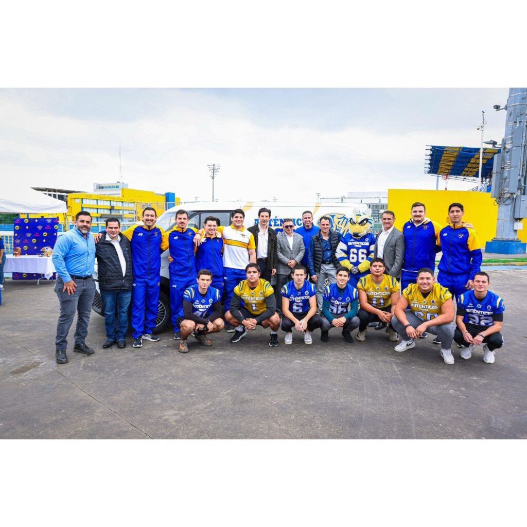 WhatsApp Image 2026-04-27 at 123042 PM - Petróleo y Energía Group of players and coaches posing outdoors in blue and yellow uniforms with a mascot and team van in the background.