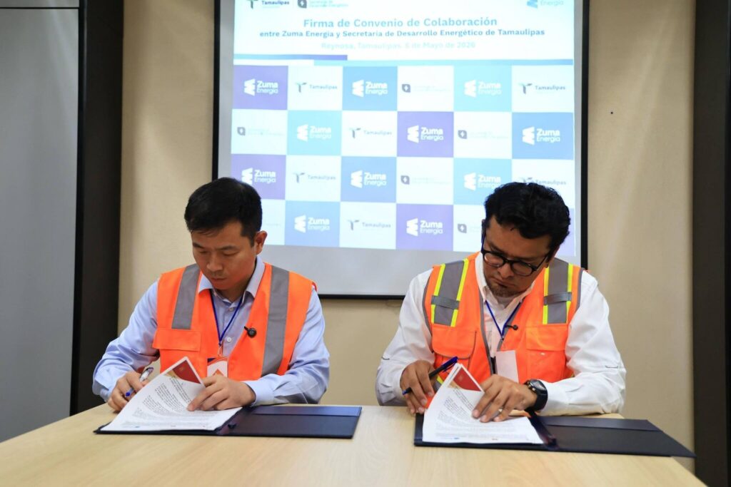 1778127200450 1 - Petróleo y Energía Two men in bright orange safety vests sign documents at a table during a formal event, with a logo backdrop behind them.