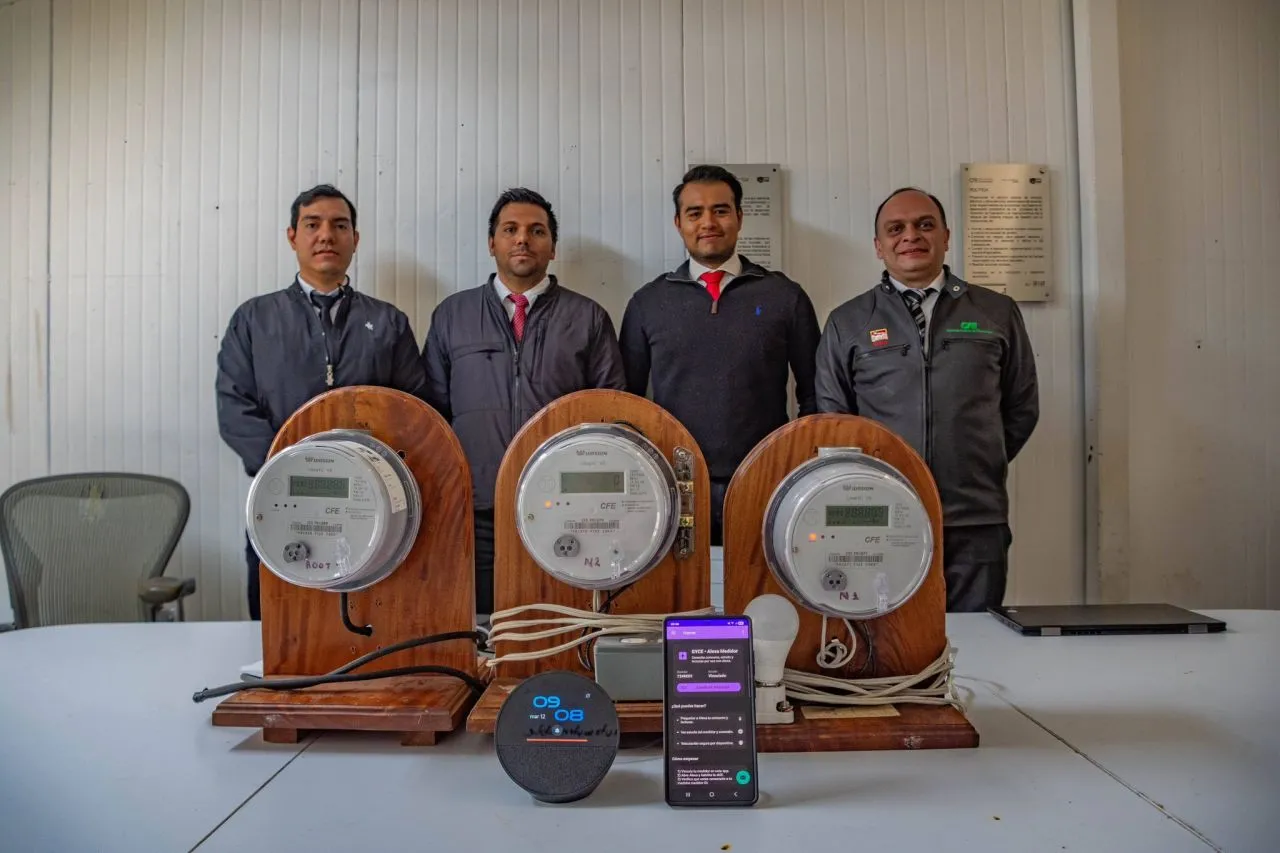 Four men in gray jackets stand behind three vintage electricity meters on wooden bases in a lab room.