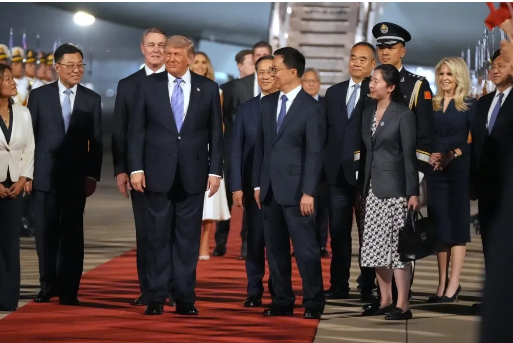 Group of formally dressed officials standing on a red carpet during a formal arrival ceremony on an airfield.