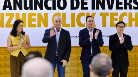 Four professionals stand on a stage, clapping, with a large banner behind them in black and yellow letters.