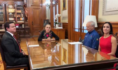 Four adults sit around a glossy wooden conference table in a formal, wood-paneled room, engaged in a meeting.
