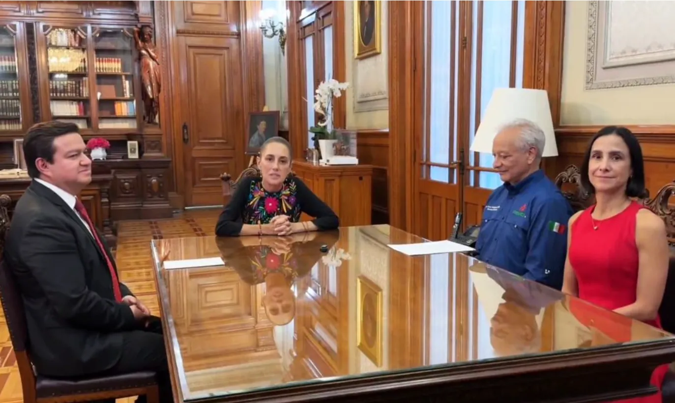 Four adults sit around a glossy wooden conference table in a formal, wood-paneled room, engaged in a meeting.