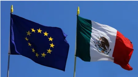 European Union flag and Mexican flag flapping in the wind against a blue sky.