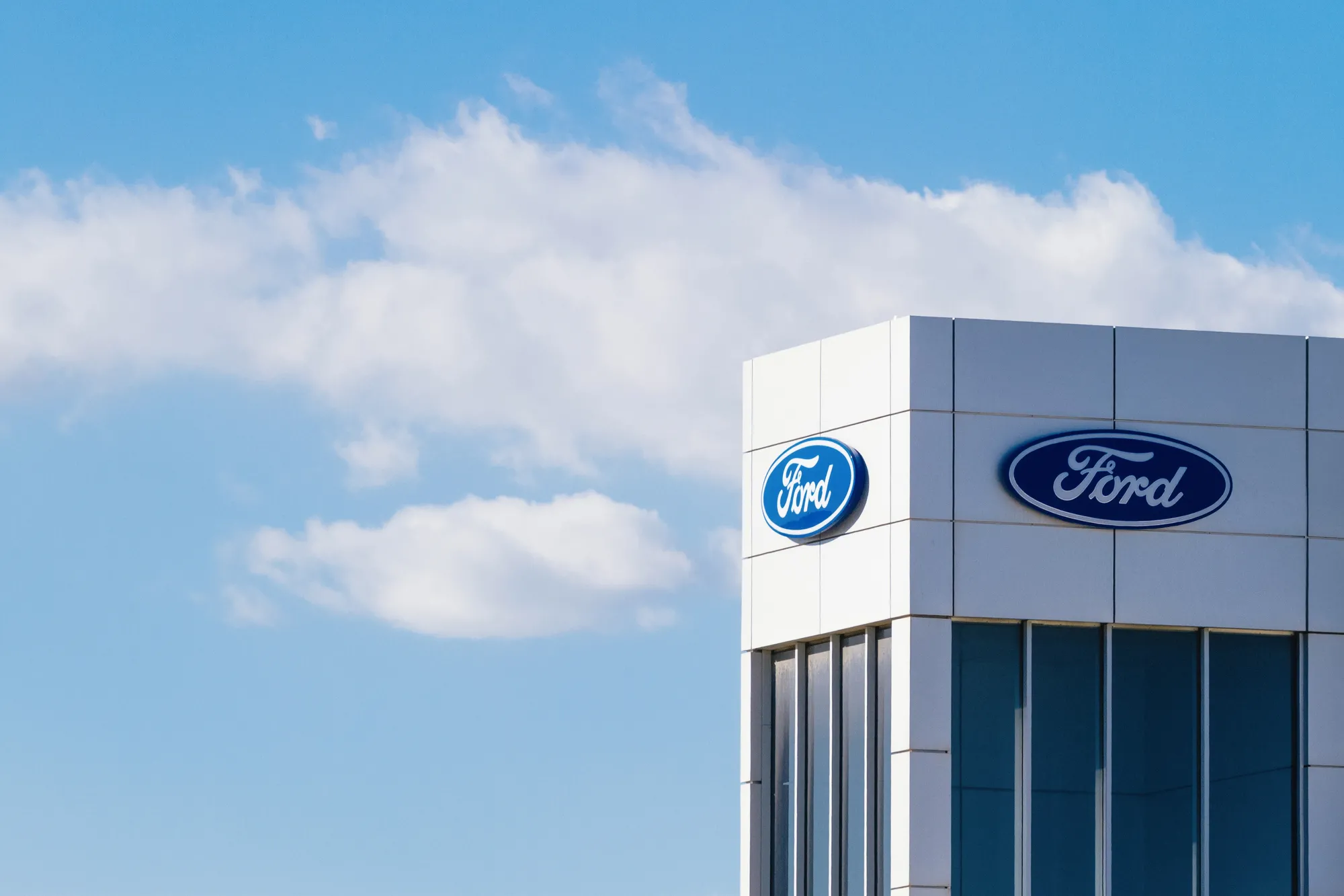 Exterior of a modern building with Ford logos on the facade against a blue sky.
