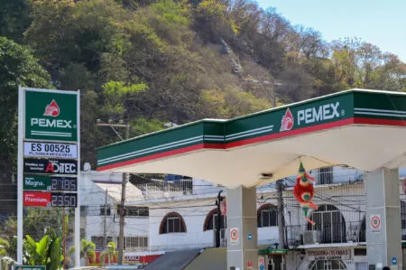 Pemex gas station with green canopy and prominent Pemex sign, hillside in the background.