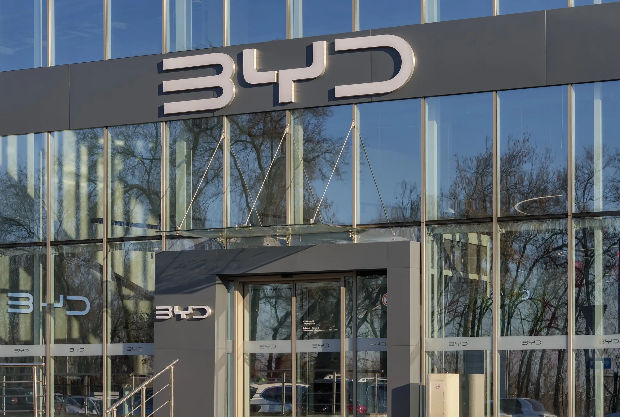 Modern glass-fronted office building with a dark gray band and large BYD lettering on the facade.