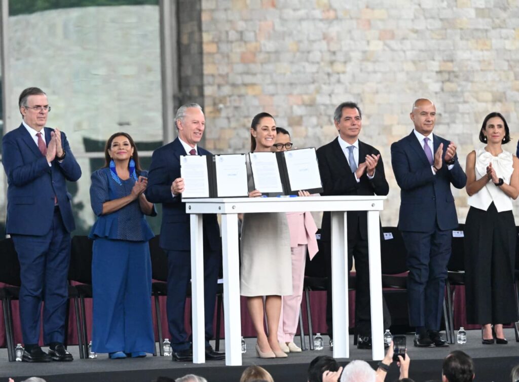 HHgr6NSWAAErwDF - Petróleo y Energía Politicians on stage signing a ceremonial agreement while others applaud.