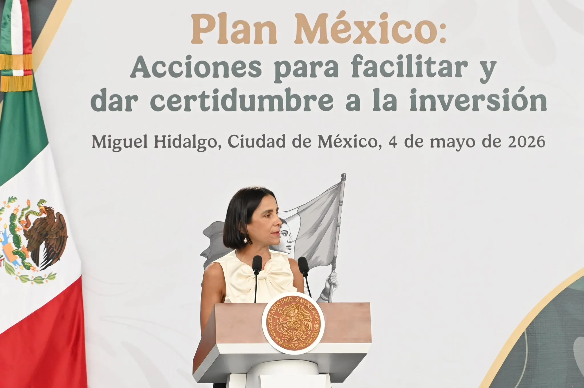 Woman at a podium giving a speech at a government event with the Mexican flag visible.