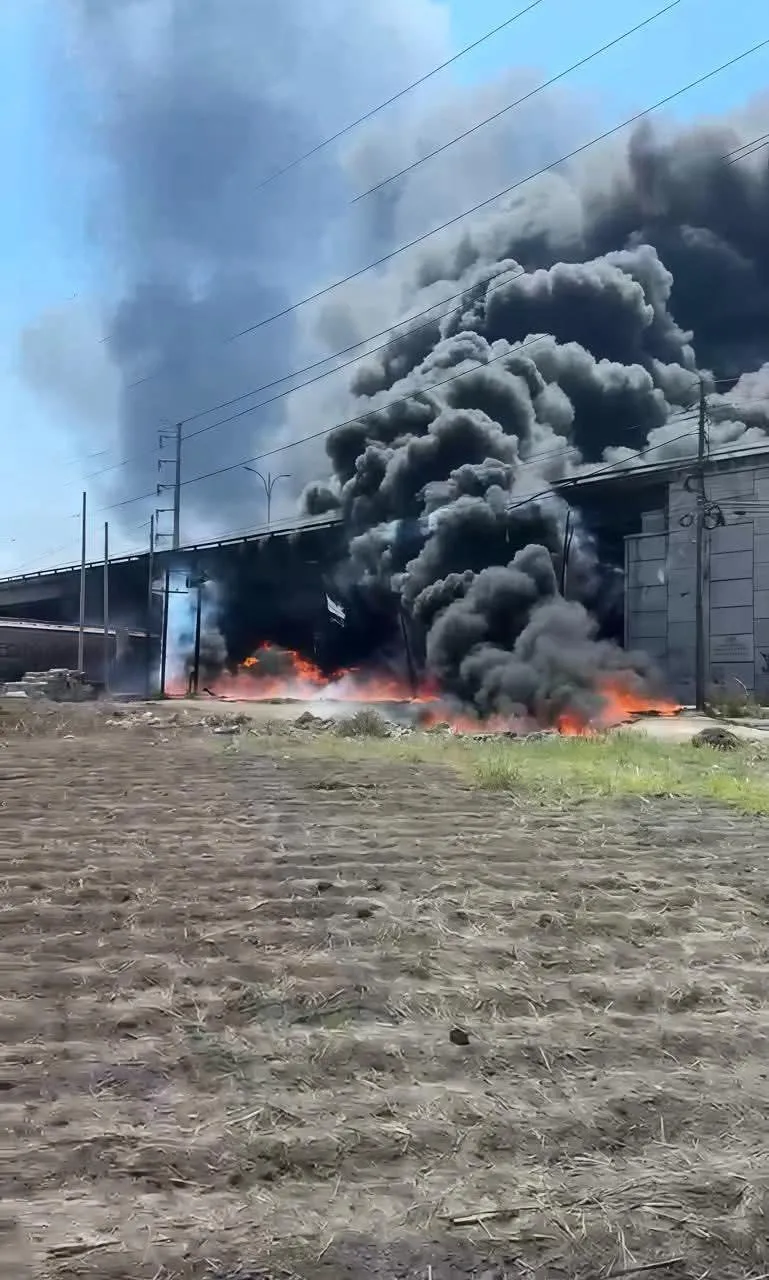 Industrial area with a large fire and thick black smoke billowing from a building/warehouse.