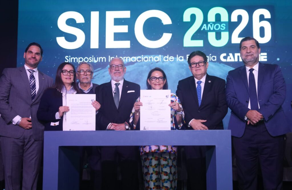 HI4hCb9WsAAk5gk - Petróleo y Energía Group of seven professionals on stage holding signed documents during a formal ceremony, with a large SIEC 2026 backdrop.