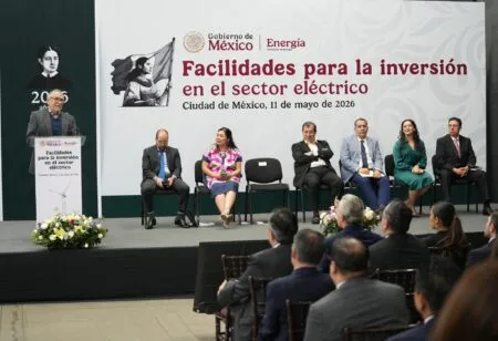 Speaker at a podium giving remarks at a government event about investment in the electric sector, with a large banner that reads 'Facilidades para la inversión en el sector eléctrico' in the background.