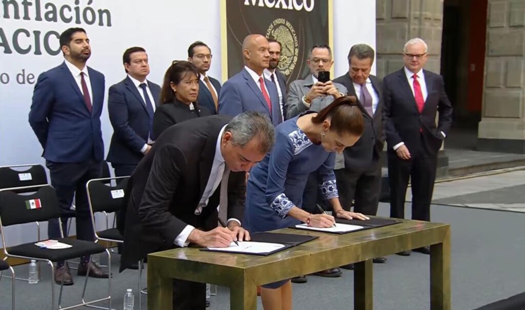 HJhFJArW0AowASz - Petróleo y Energía Two officials sign documents at a formal signing ceremony, a man in a dark suit and a woman in a blue dress with others observing behind them.