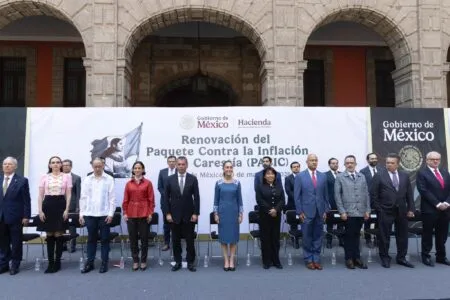Group of formally dressed officials standing in front of a banner at a government event, with stone arches in the background