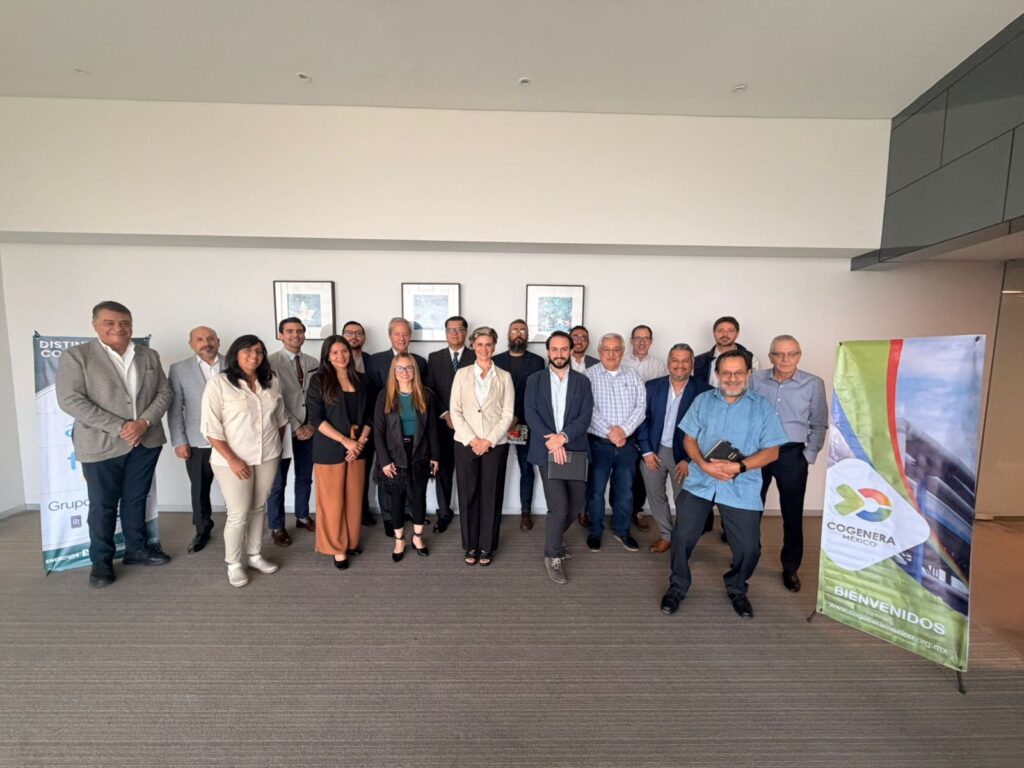 WhatsApp Image 2026-05-12 at 120812 PM - Petróleo y Energía Group of professionals in business attire posing for a photo at an indoor event, banners visible on both sides of the room.