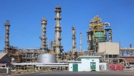 Industrial refinery with tall distillation columns and extensive piping against a clear blue sky.