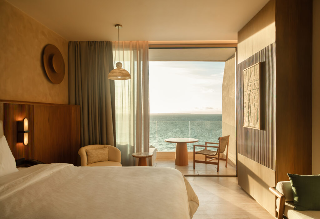 02 - Petróleo y Energía Hotel room with a bed in the foreground and a sea view through a large window.