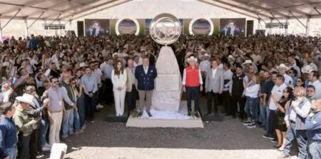 Large crowd gathered under a white canopy around a central stone monument with a circular emblem on top, at a ceremonial event.