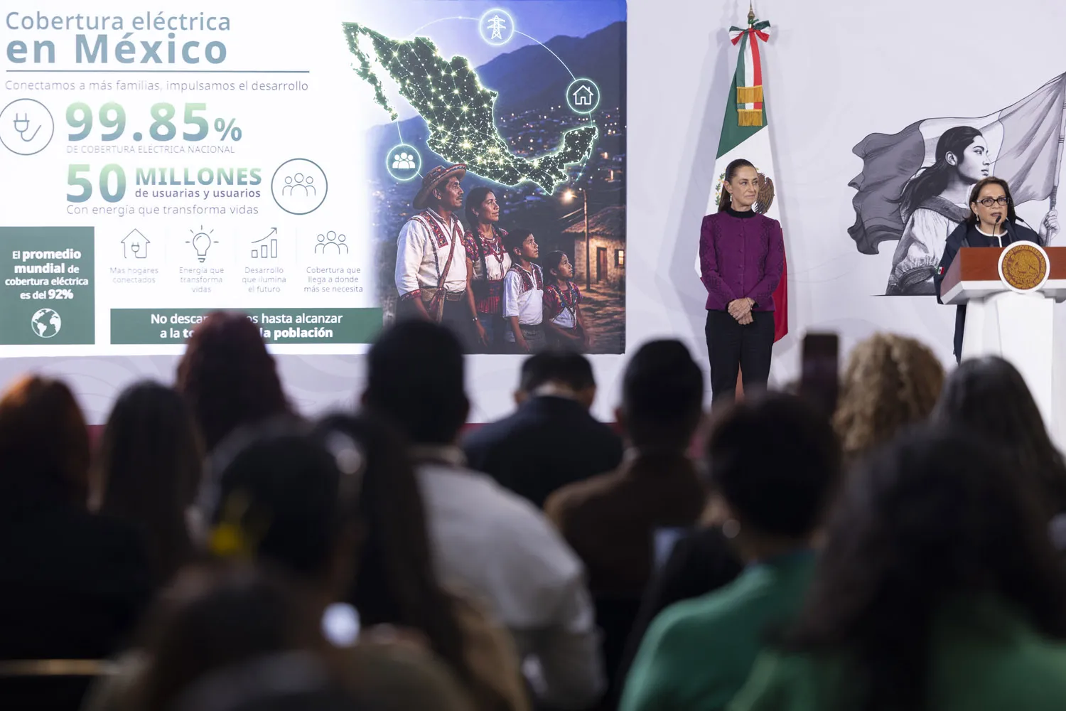 Speaker at a podium during a conference about electrical coverage in Mexico, with a large infographic banner and the Mexican flag in the background.