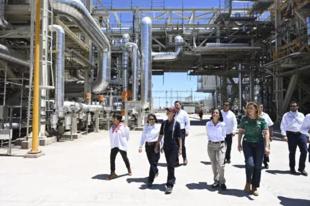 Group of professionals walking through an industrial facility with extensive silver piping and steel framework, on a site tour.