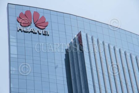 Tall glass office building with the red Huawei logo visible in the upper left corner against a clear blue sky.