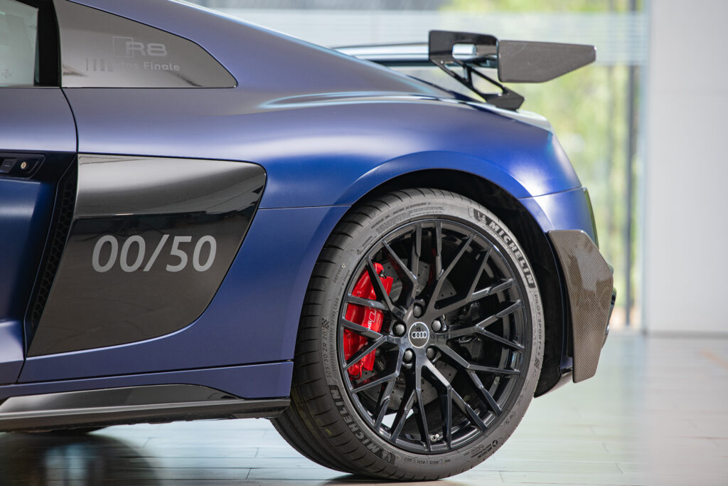 wwwalexbertheaucom - Petróleo y Energía Close-up of a blue Audi R8 race car wheel with red brake calipers and carbon fiber aero parts nearby