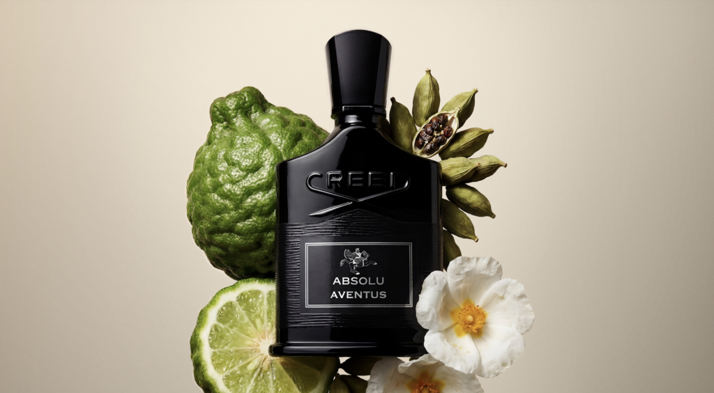 Aventus 4 - Petróleo y Energía Creed Absolu Aventus perfume bottle centered, surrounded by green citrus fruit and white flowers.