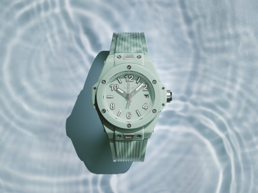BIG BANG MINT GREEN CERAMIC 2 - Petróleo y Energía Close-up of a mint-green wristwatch against a blurred blue water background, showcasing the dial and strap.