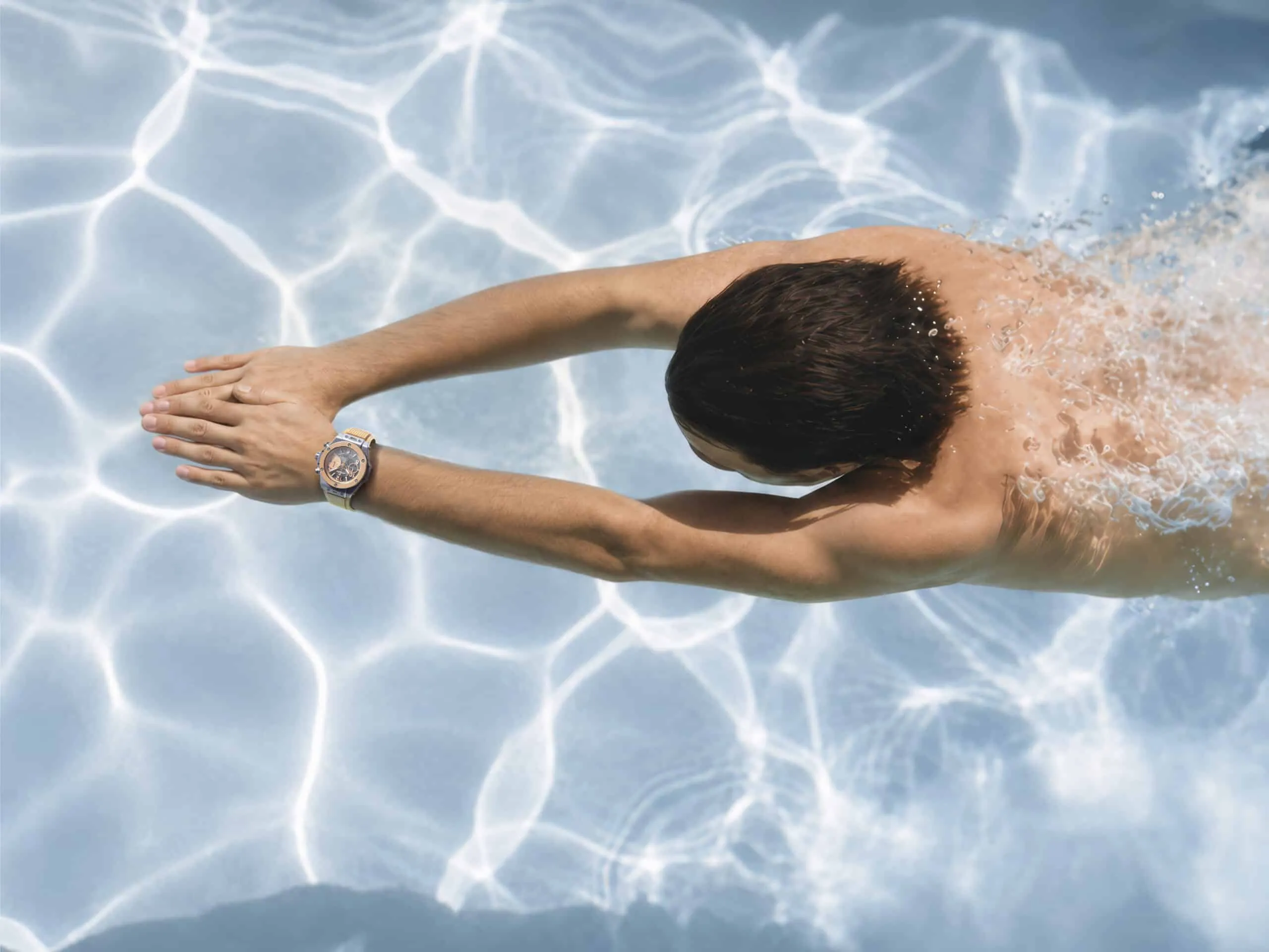 Person swimming in a pool with arms extended forward, wearing a watch on the left wrist.