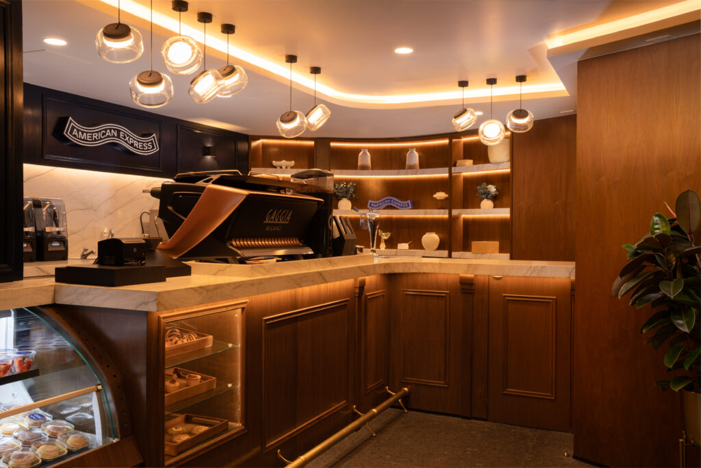 BLUE-ROAST_3046-Edit 1 - Petróleo y Energía American Express cafe counter with a copper espresso machine, glass pastry case, and warm wood shelves