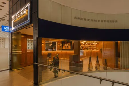 American Express storefront in a shopping mall with glass railing and warm interior lighting.