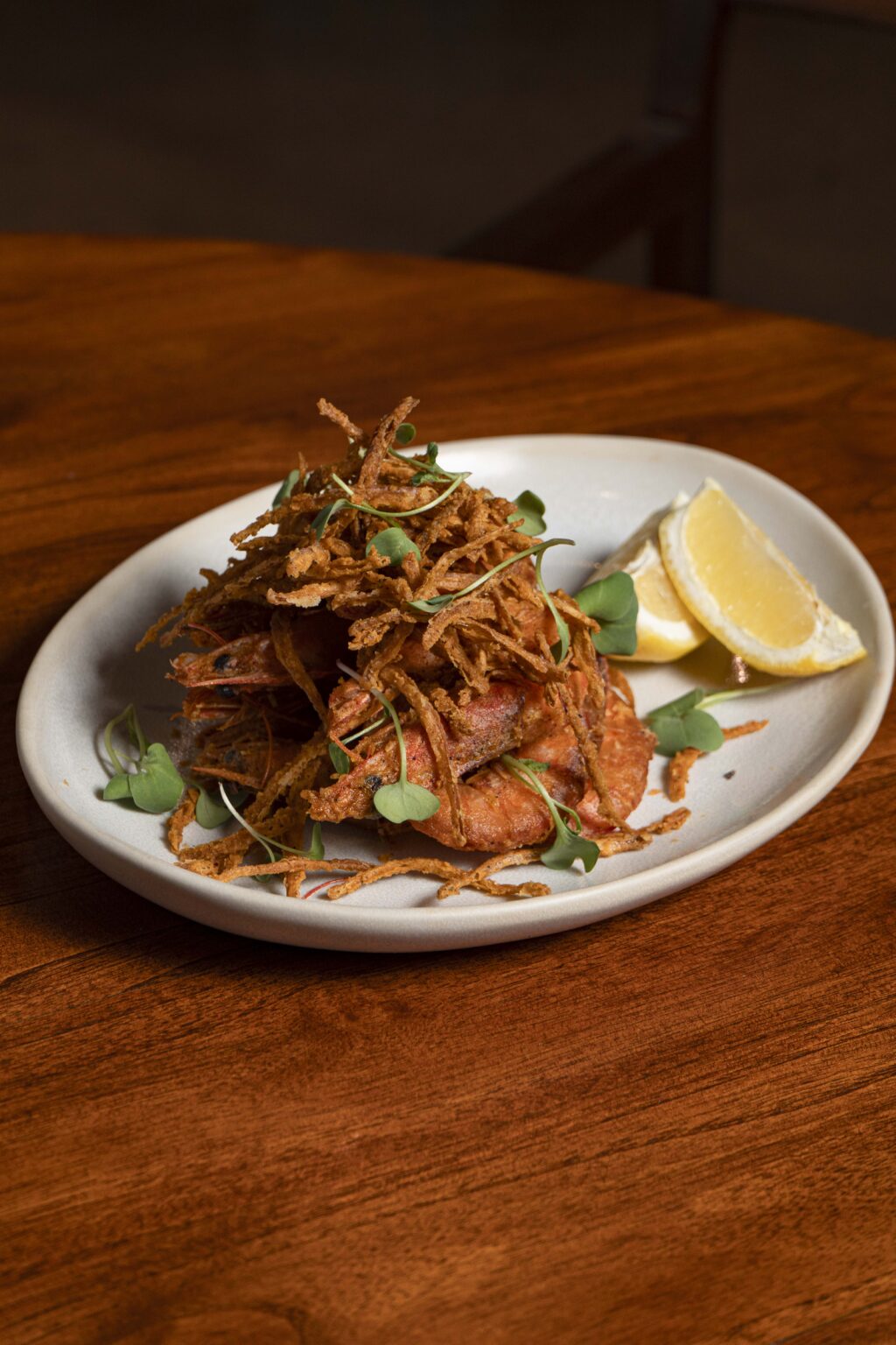 CASCABEL_mayo 2025_95 - Petróleo y Energía Plate of fried shrimp topped with crispy onion strands and microgreens, with lemon wedges on the side.