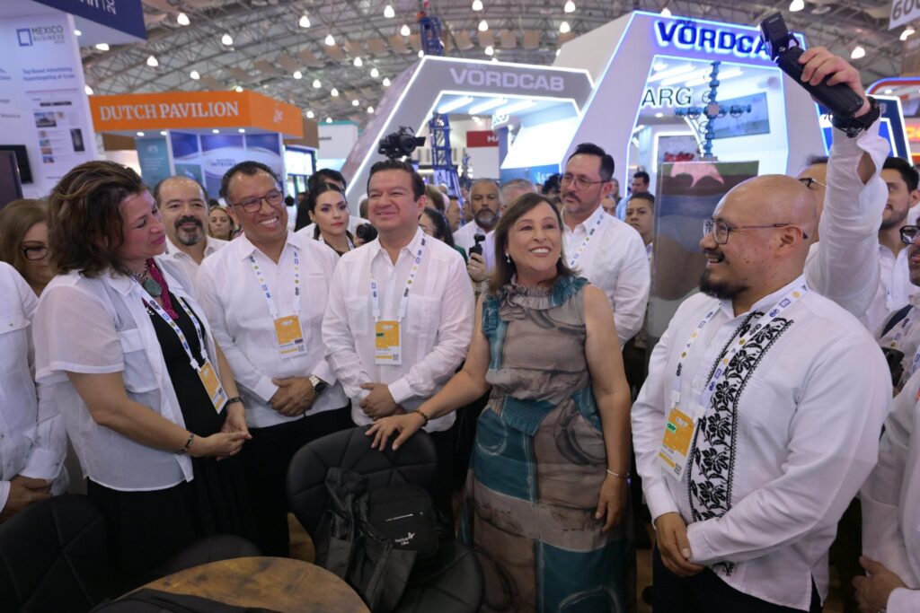 CMP recorrido piso - cortesia - Petróleo y Energía Group of professionals at a convention posing for a photo, expo booths in the background and badges visible on lanyards.
